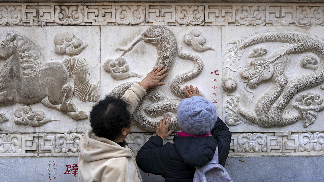 Women touch the snake figure on the stone wall ahead of the Chinese Lunar New Year of the Snake, following the Chinese zodiac, as people visiting the Baiyun Taoist Temple in Beijing, Wednesday, Jan. 22, 2025.