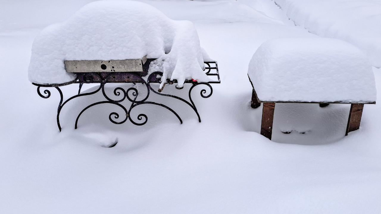 A grill and garden table covered in deep, fresh snow.